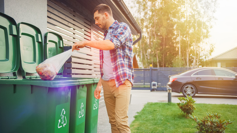 A man is throwing trash away in large outdoor garbage cans