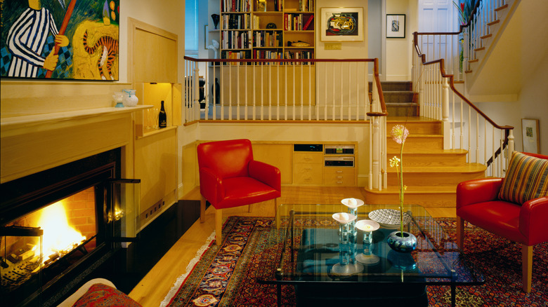 A sunken living space with red chairs, timber trims, a fireplace and a bookcase in the background