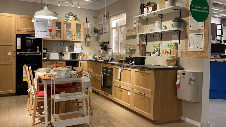 A cozy modern kitchen showroom with wooden cabinets, plants, and kitchenware neatly arranged. Ikea showroom Sentul.