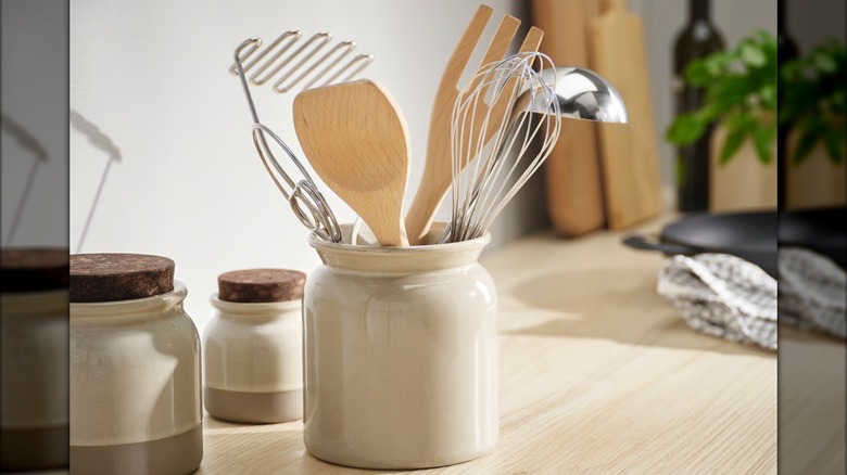 A beige stoneware jar holding kitchen utensils over an engineered wood countertop