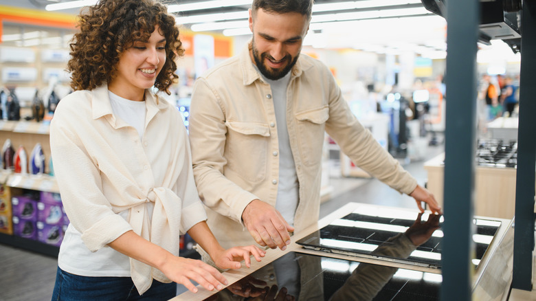 Happy couple selecting a new induction stovetop, enjoying their shopping experience in a modern home appliance store