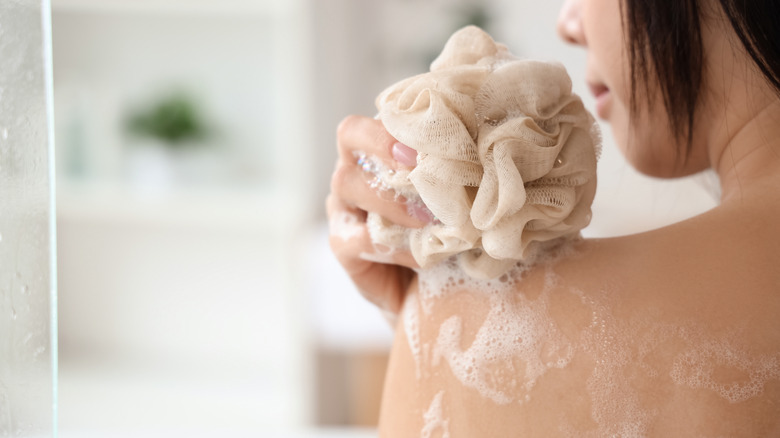 person using loofah on shoulder in shower