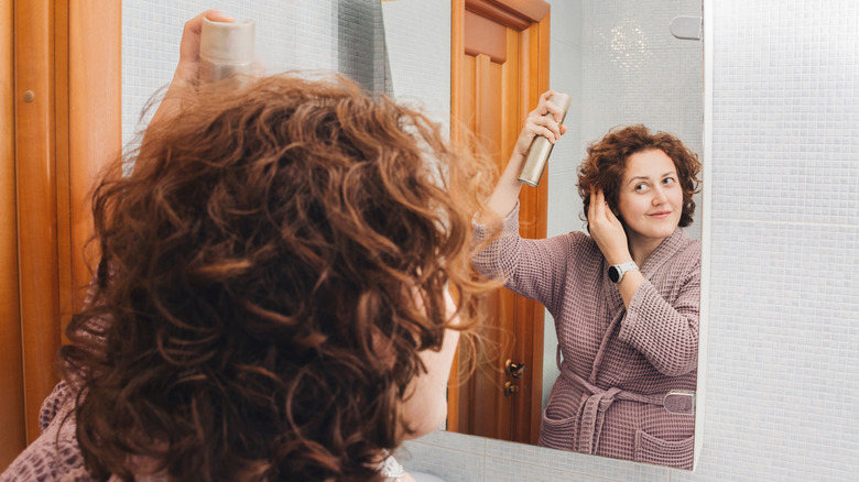 Woman using hairspray in bathroom