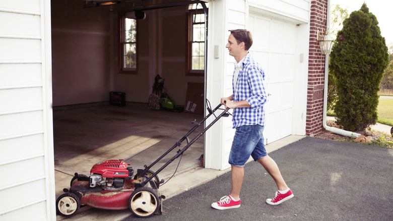 Man pushing a red lawn mower into the garage