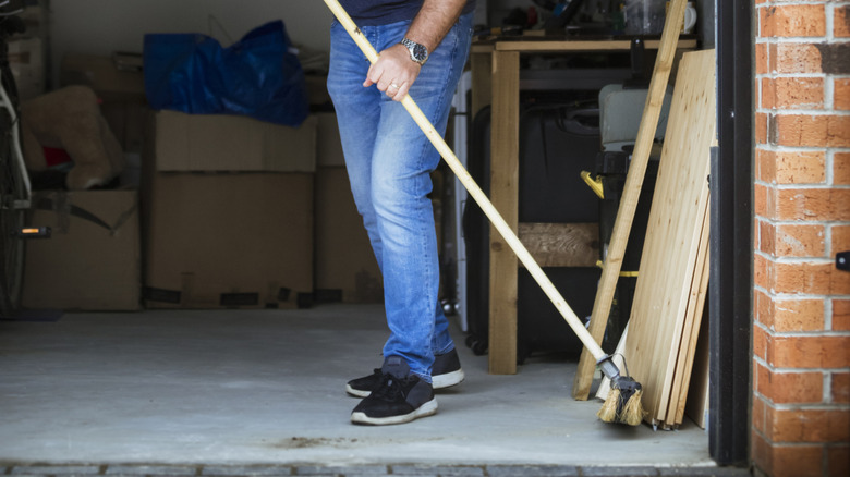 Man holding a push broom in a garage