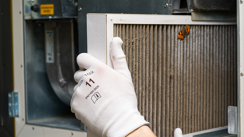 A gloved hand removing a dirty HVAC filter.