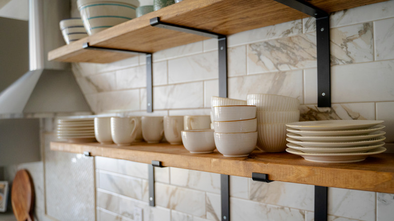 A close-up of open kitchen shelves with cups and plates and exhaust hood.