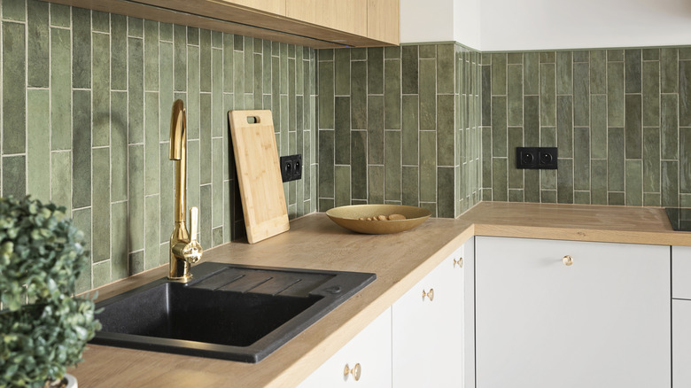 Interior of kitchen with furniture with modern handle, green tile and kitchen sink with faucet.