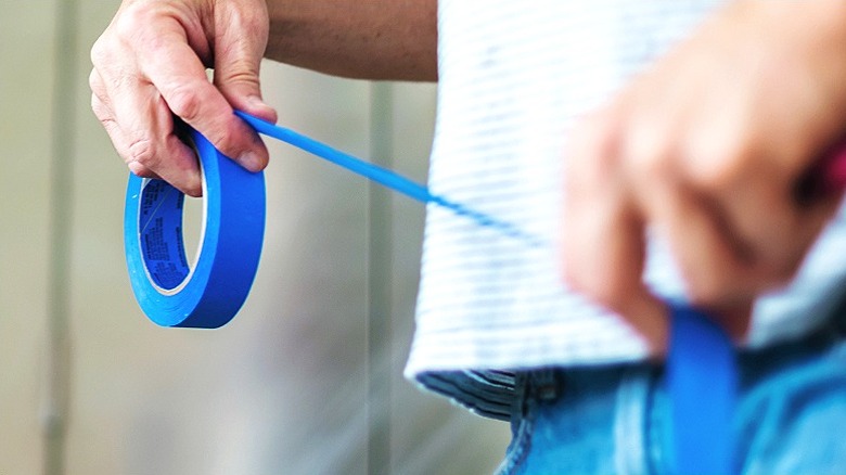 A close-up of a person's hands pulling a length of blue painter's tape from the roll