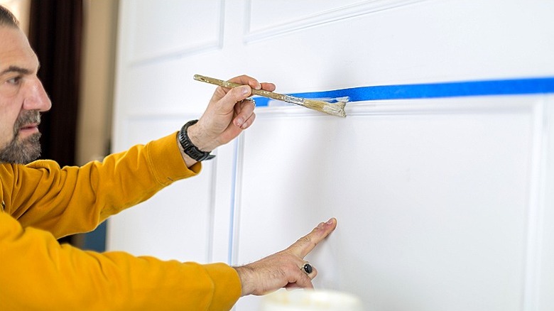 Person painting a wall trim using blue painter's tape