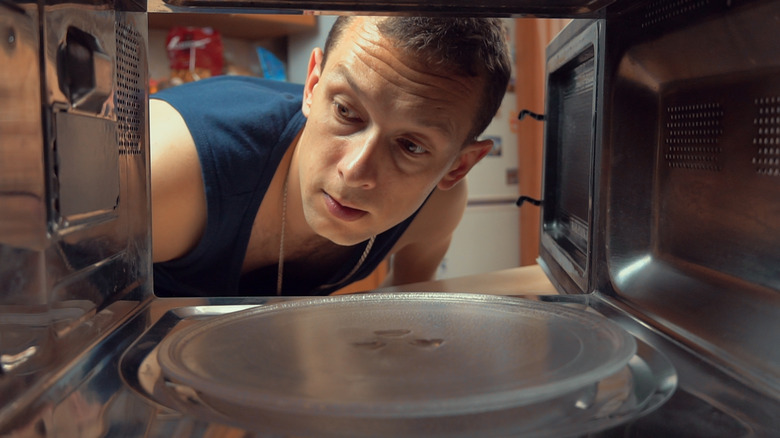 A man looks nervously inside his microwave