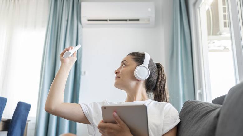 Woman sitting on a couch with headphones on and holding a remote control pointed at her AC unit