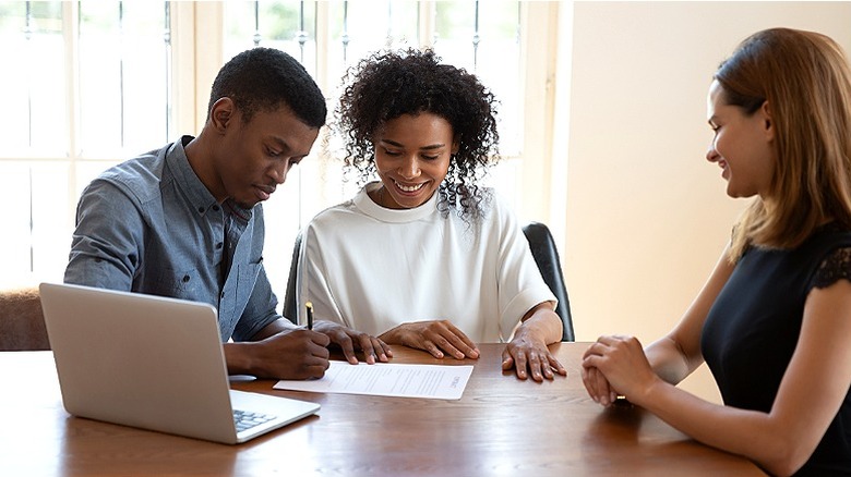 Man and woman sign contract at a table with an agent sitting next to them