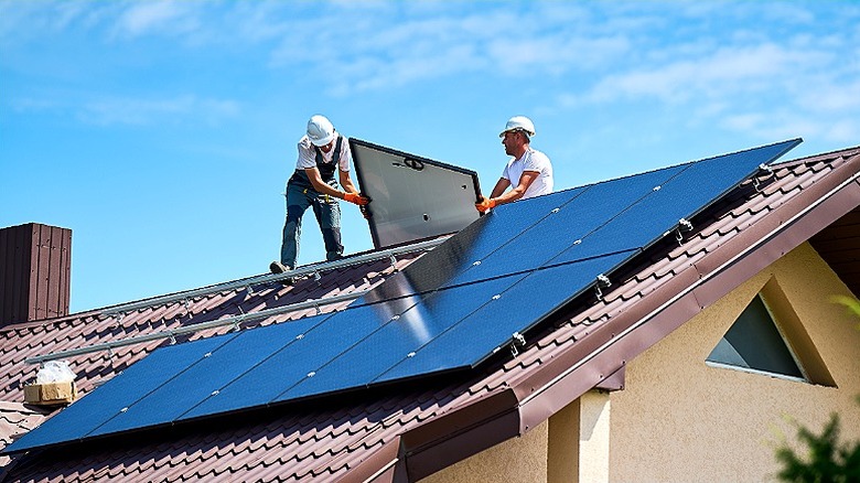 Two professionals wearing hard hats install solar panels onto roof