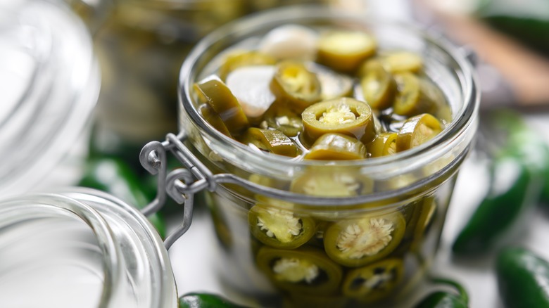 Spicy jalapeños are being stored in a glass jar with a sealable lid.