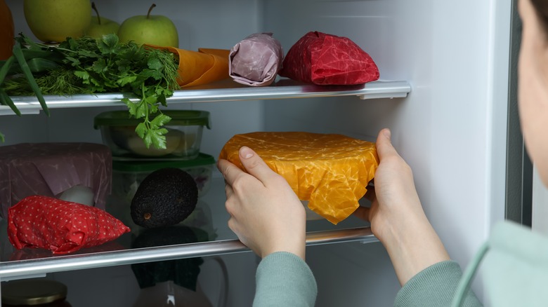 Multiple food items are being stored with beeswax fabric wraps in a refrigerator.