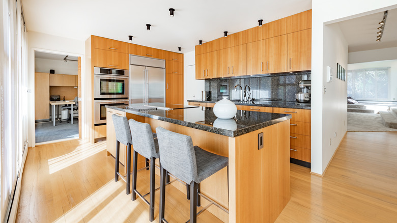 Scandinavian-style clean kitchen interior with black marble granite countertops, tall wooden cabinets, wood flooring, and an island with three barstools.