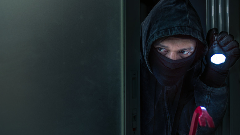 Masked burglar holding a crowbar in one hand and a torch in the other