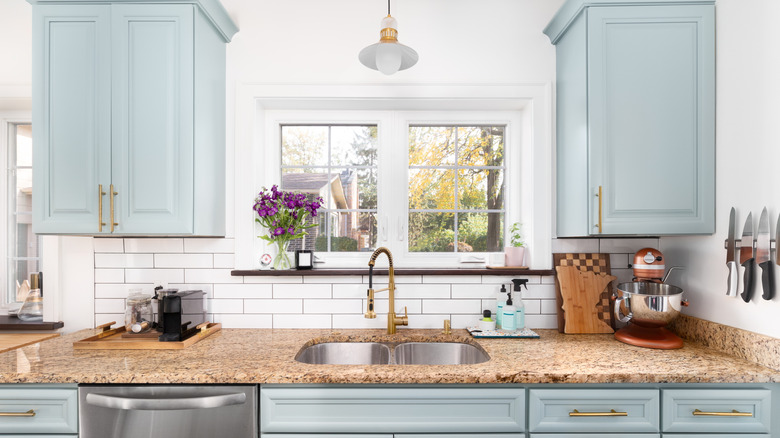 Light blue kitchen cabinets with gold handles and white backsplash