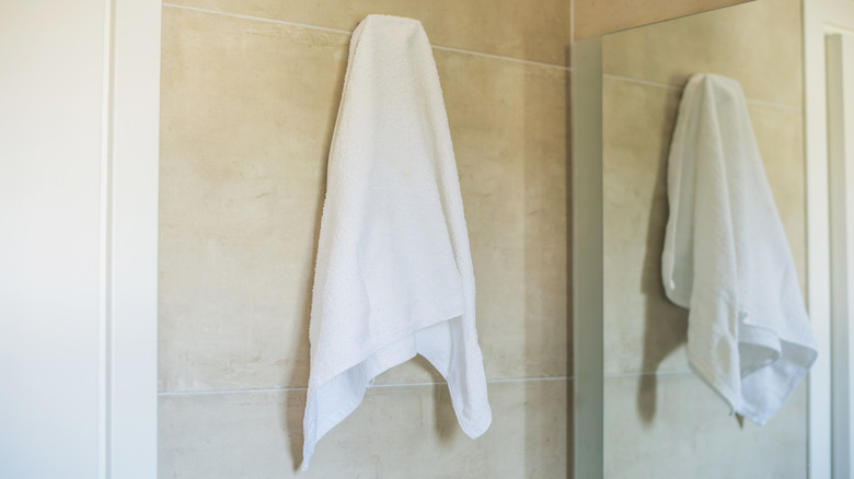 A white bathroom towel is hanging up in the bathroom, reflected by a nearby mirror.