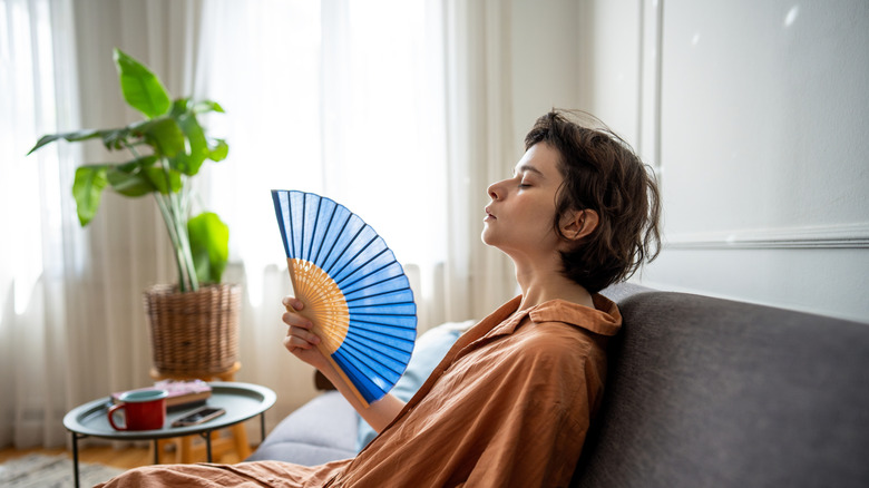 Woman on a couch fanning herself with a blue fan
