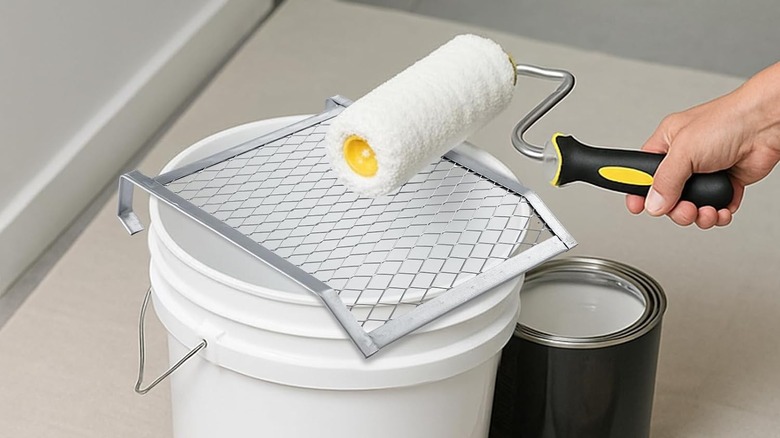 Hand holding a paint roller above a bucket with a roller grid on top