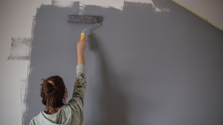 Woman using a roller to paint a wall gray