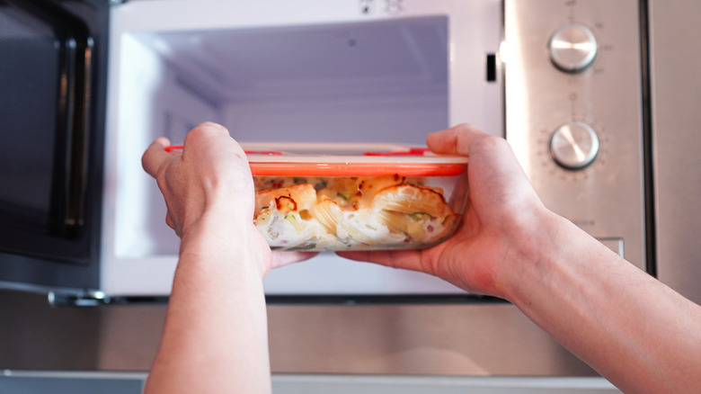 Close up of person putting glass food container into microwave