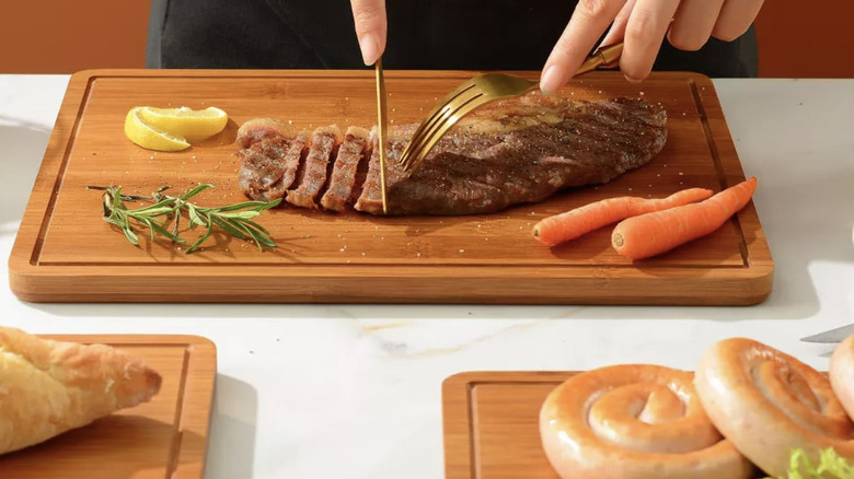 A person cuts meat on a carbonized bamboo cutting board