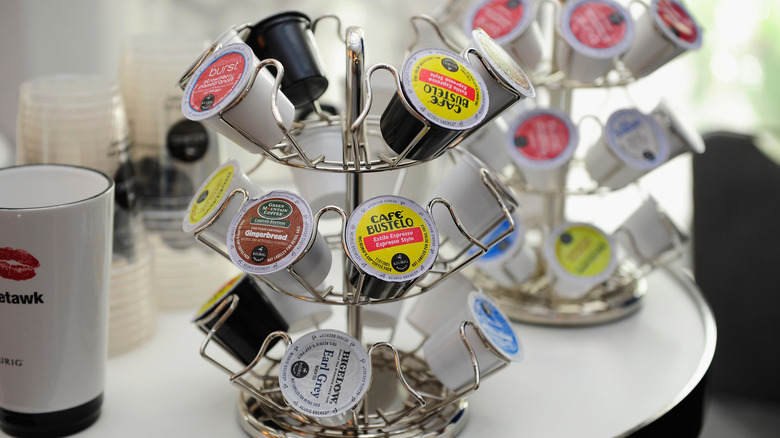 Metal Keurig cup holder with several spaces filled with either tea or coffee, set on a table next to a cup