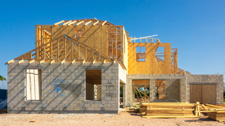 A large brick home under construction with timber framing on upper level and timber roof trusses
