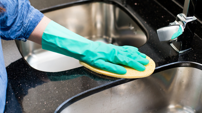 A gloved hand cleaning an undermount kitchen sink with a sponge