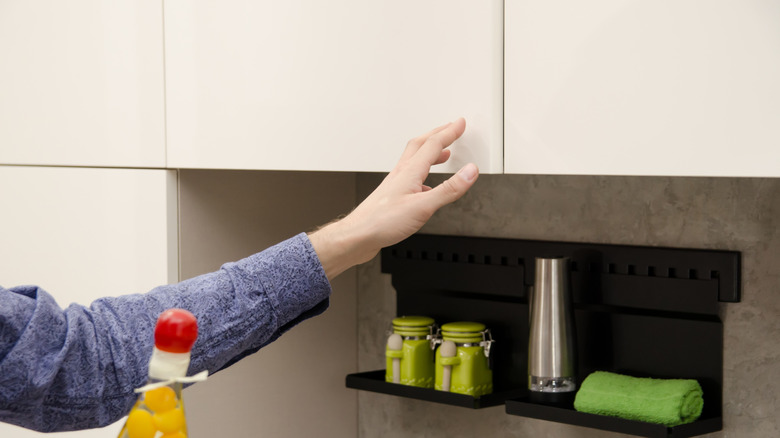 hand placed on cream push-to-open cabinets in kitchen with green salt and pepper shakers