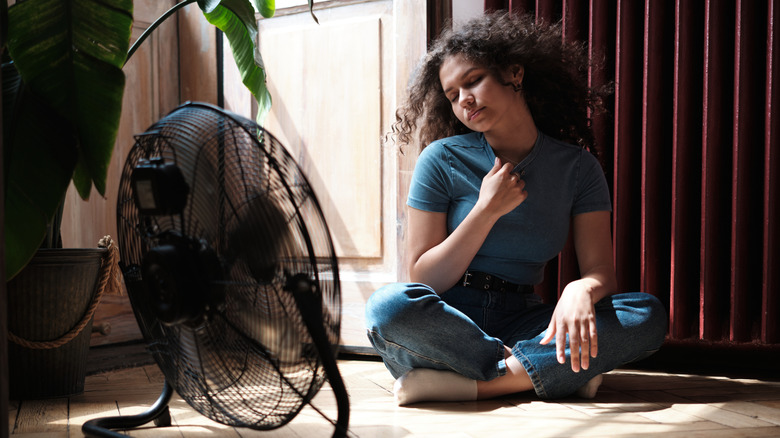 A young woman with a fan and window curtains down during a heat wave