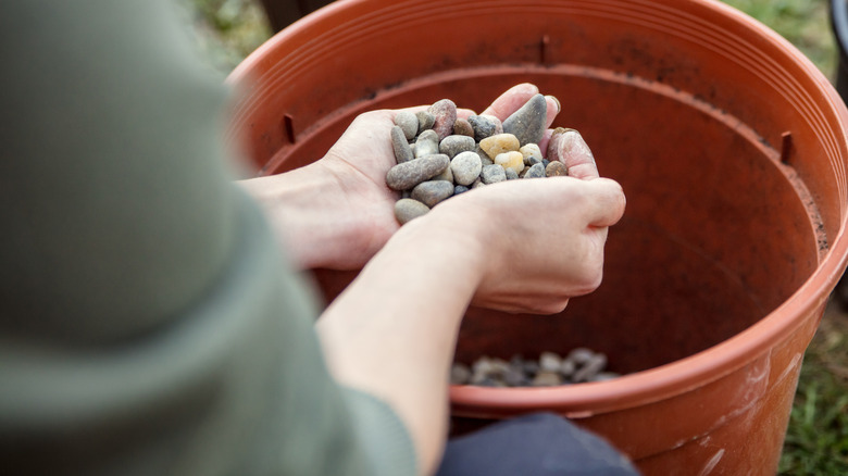 Someone holding pebbles over a bucket