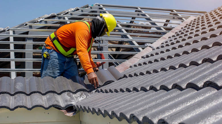 Construction worker standing on a roof covering it with new tiles.