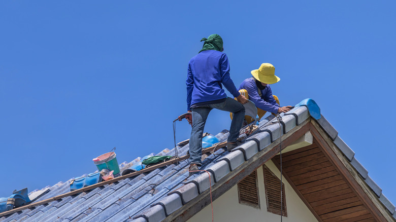 Workers repairing leaking ridges tile roofing and replace cracked broken tile roofing on blue sky background.