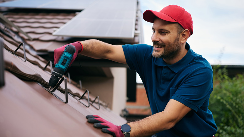 A roof installer smiles while using a hand tool to position the new roof.