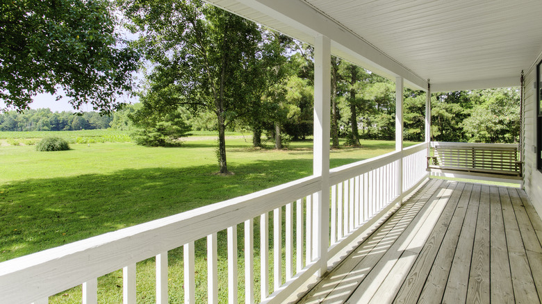 View from a wrap-around porch onto a green yard with trees.
