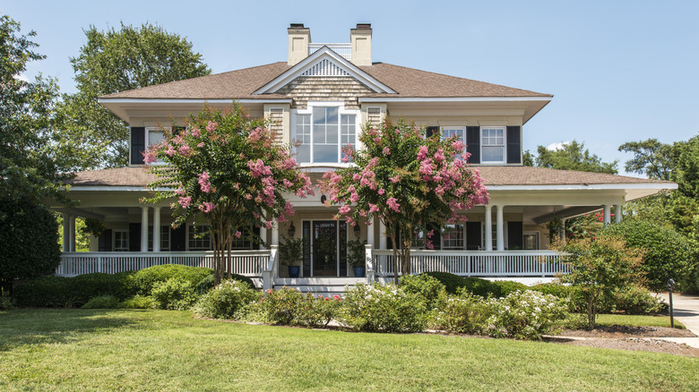 Exterior of a Southern home with a wrap-around porch, framed by flowering trees.