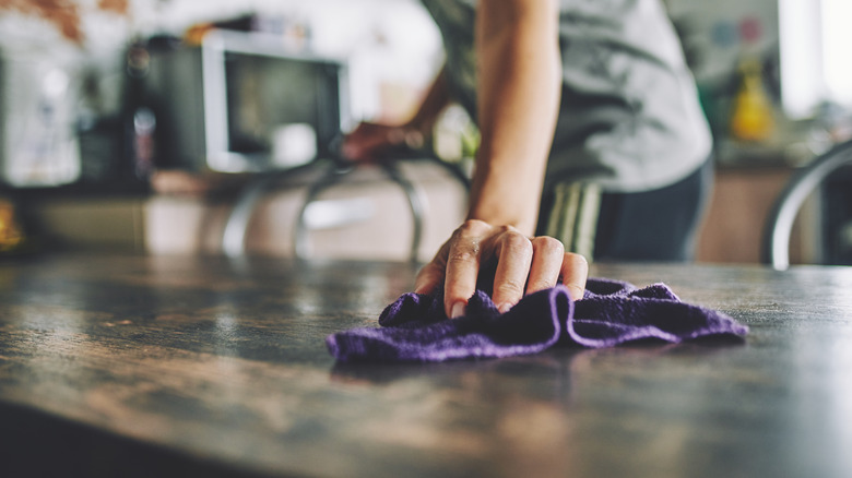 A person's hand wiping a table with a purple cloth