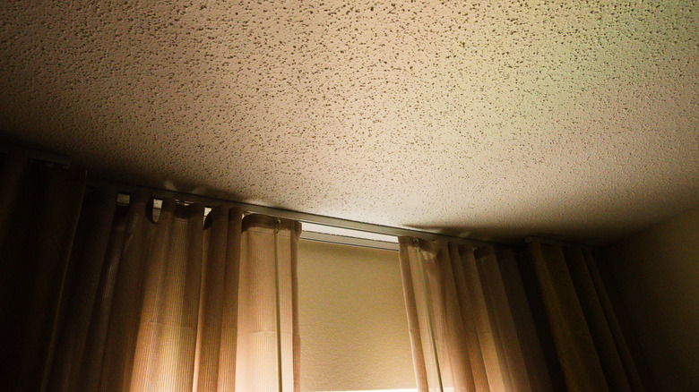 A popcorn ceiling lit up tan by evening light shining through drawn beige curtains.