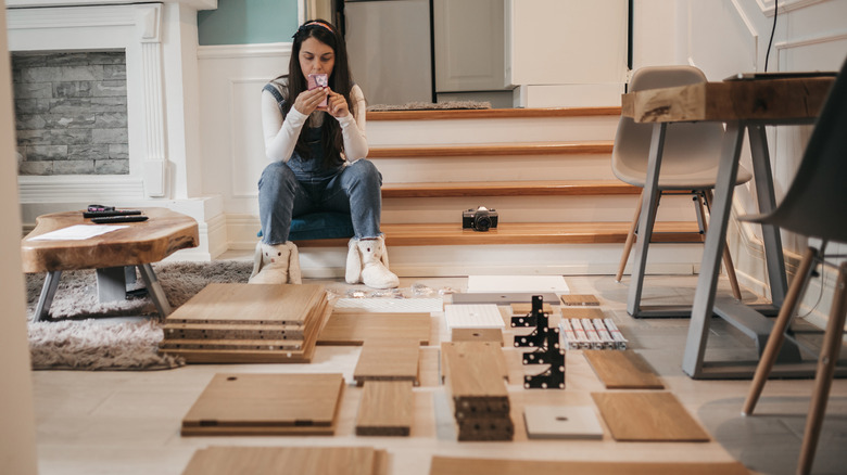 Woman sitting on steps using her phone, pieces of furniture organized for assembly