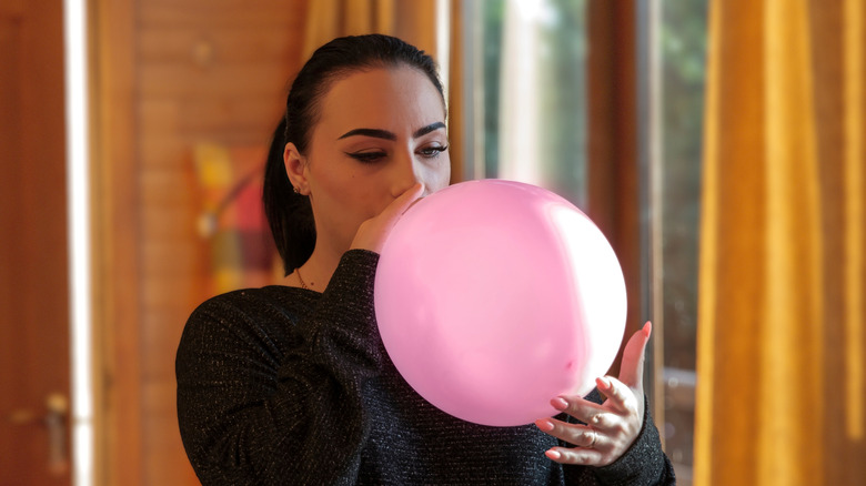 A woman blowing up a pink balloon.