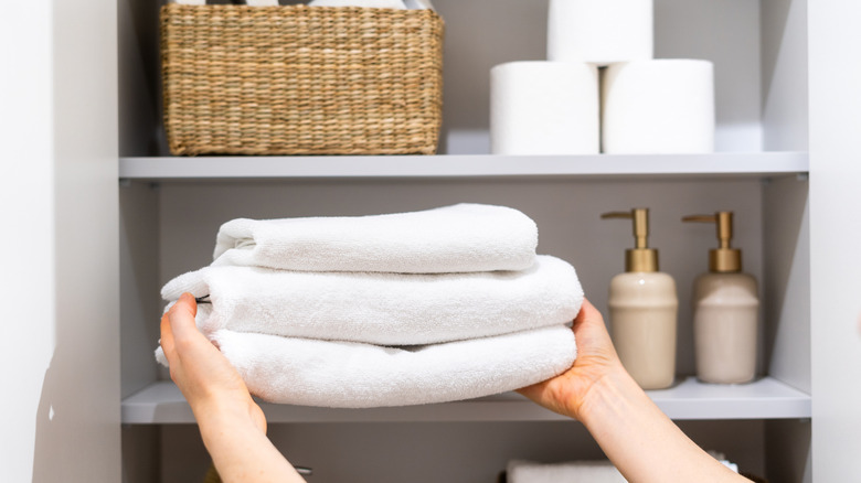 A woman placing towels in a linen closet.