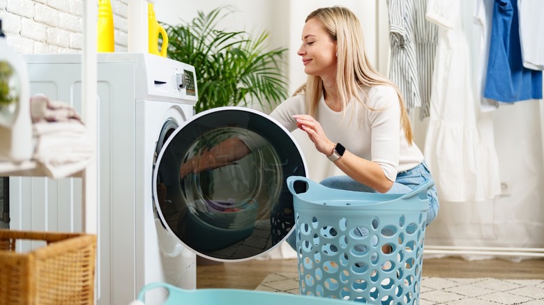 woman putting laundry from white washing machine into blue basket