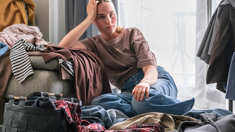 Woman looking overwhelmed sitting in the middle of clothes