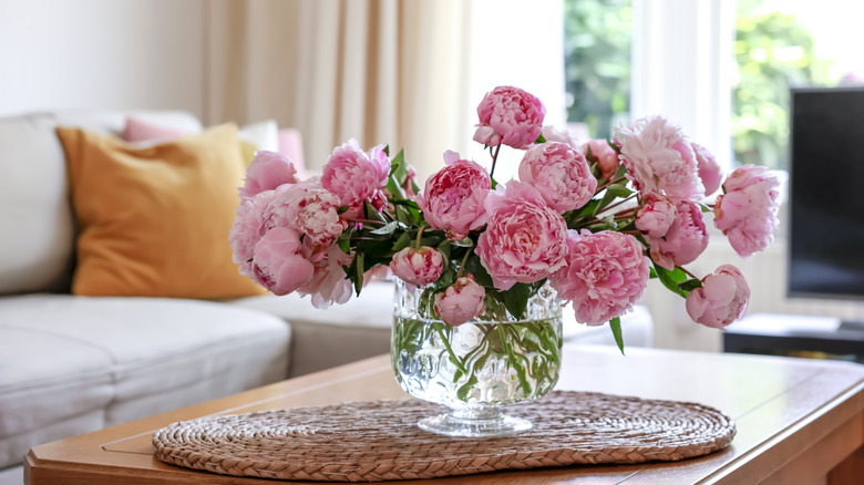 Pink peonies sitting in a glass vase in a living room