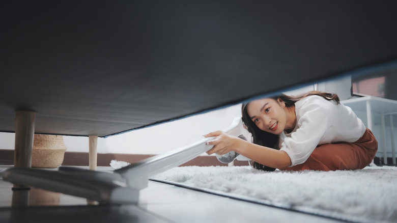 A woman vacuuming the space beneath her living room sofa