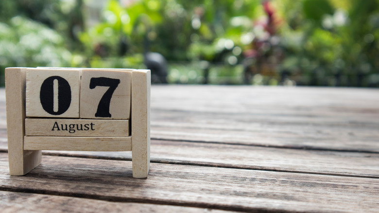 Wooden cube calendar showing August 7 on a wooden table outside